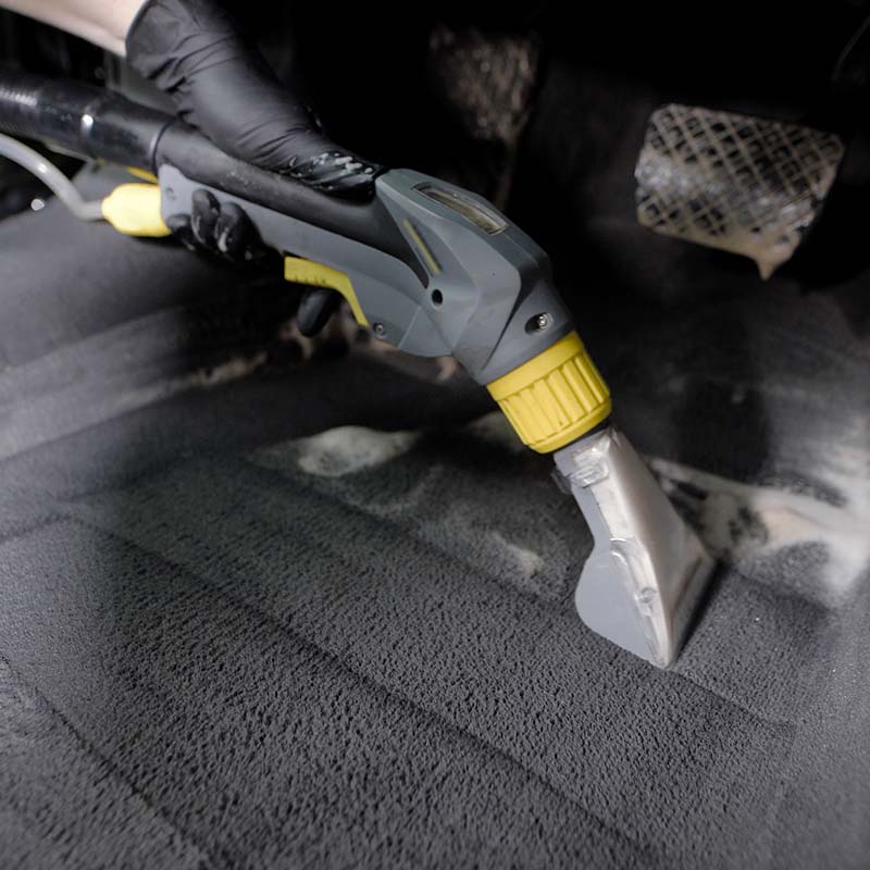 Autowäscher saugt Fußmatte im Auto mit einem Staubsauger